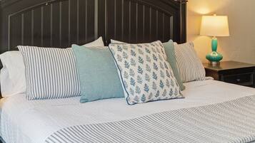A bed with a striped bedspread and multiple pillows, a dark headboard, and a nightstand with a lamp.