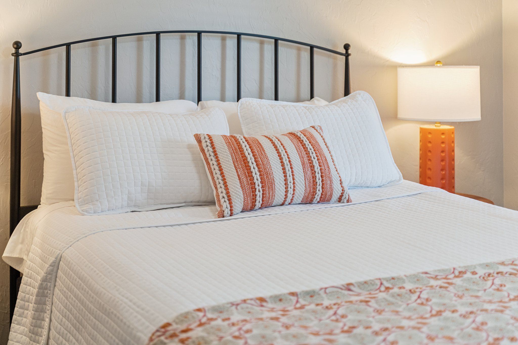 Een bed met een metalen frame, witte beddengoed en een geborduurd plaid.