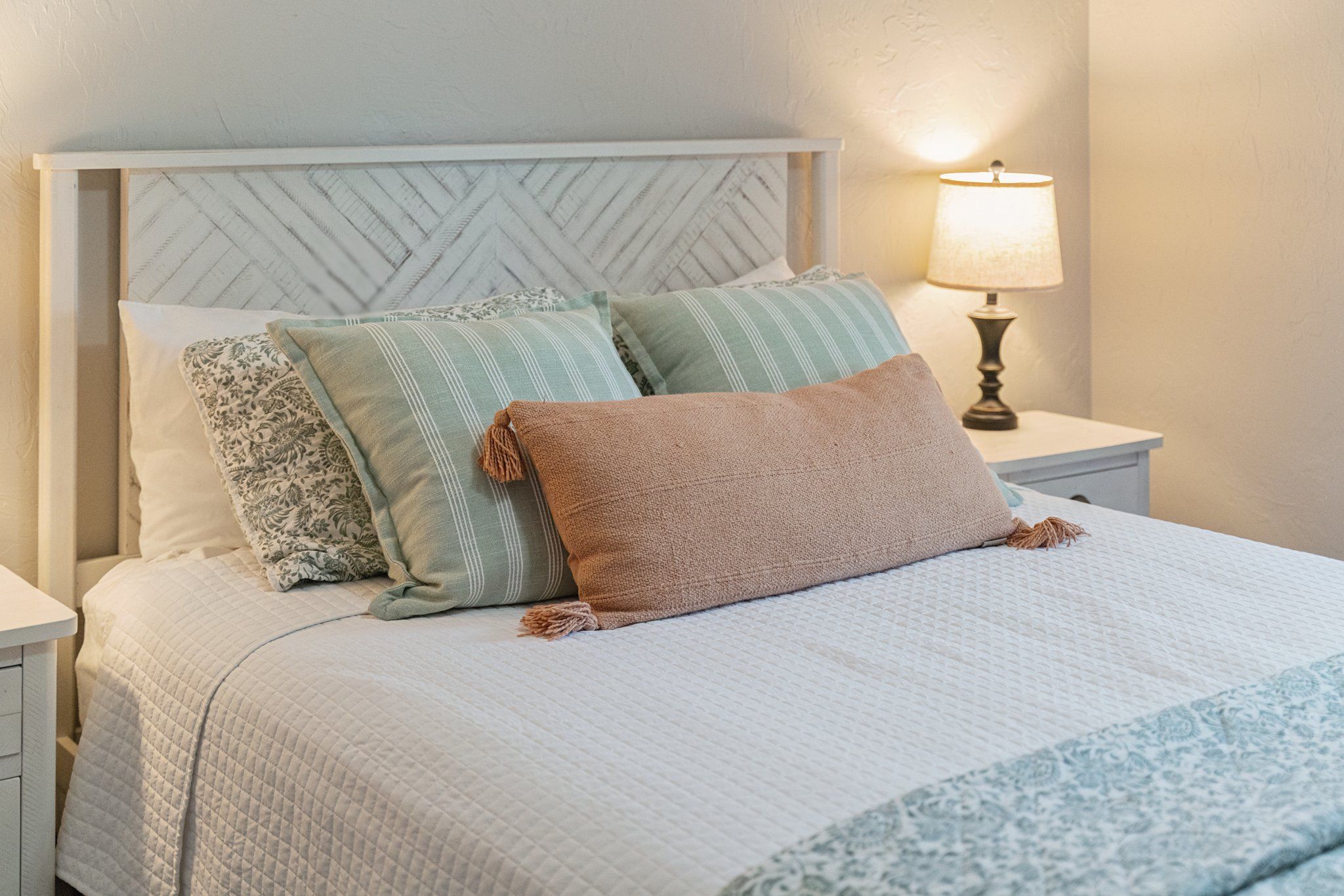 A bed with a quilted bedspread, a headboard with a herringbone pattern, and two bedside lamps.