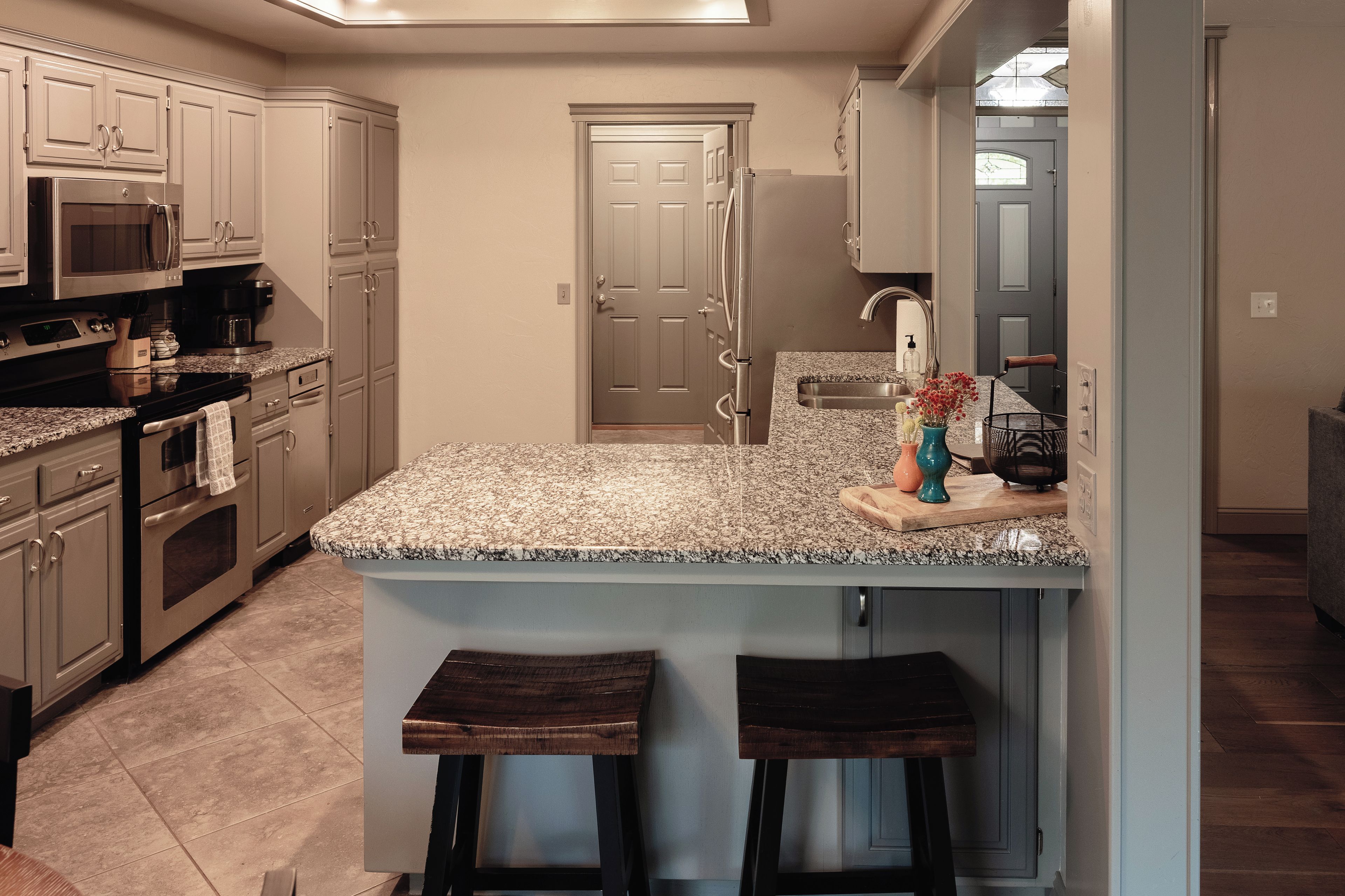 Una cocina con encimera de granito, electrodomésticos de acero inoxidable y un taburete de bar de madera.