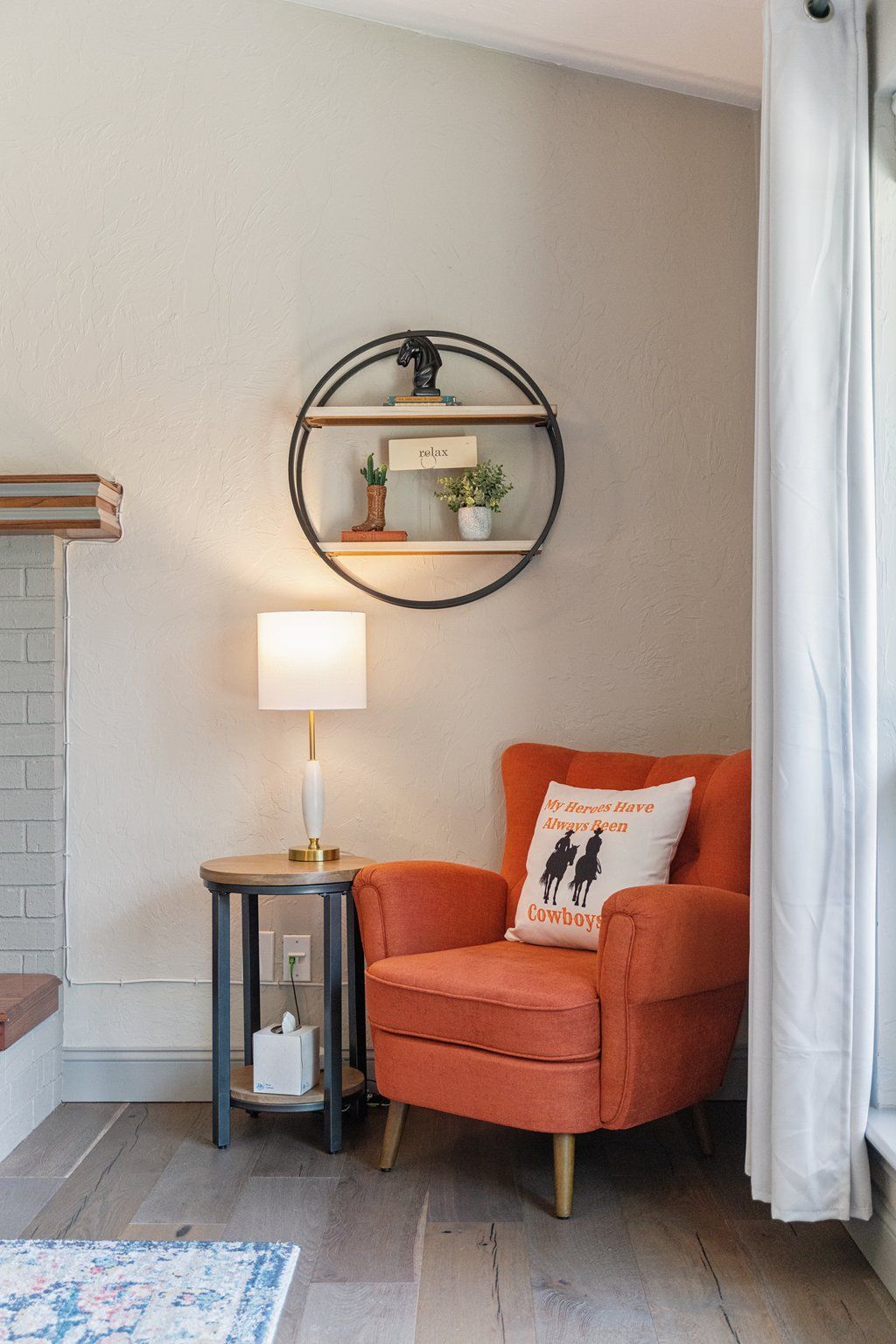 A cozy corner with a round wall shelf, a lamp, a cushioned chair, and a decorative pillow.