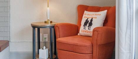 Un rincón acogedor con un estante redondo en la pared, una lámpara, un sillón mullido y un cojín decorativo.