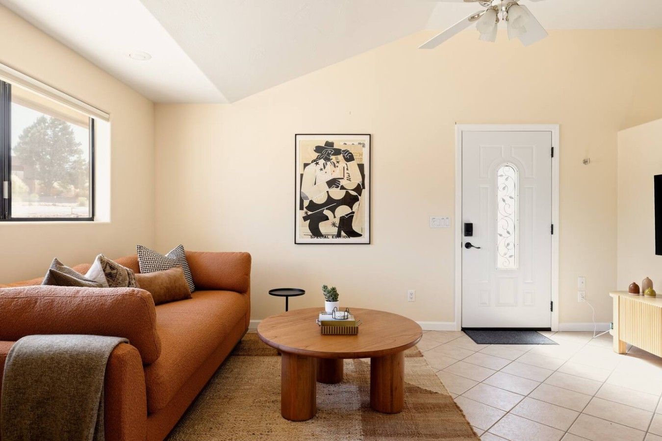 A living room with a sofa, a round wooden coffee table, a door with decorative glass panels, and a framed artwork on the wall.