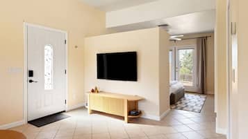 A modern living room with a flat-screen TV mounted on the wall, a wooden console table, and a large window offering a view of the outdoors.