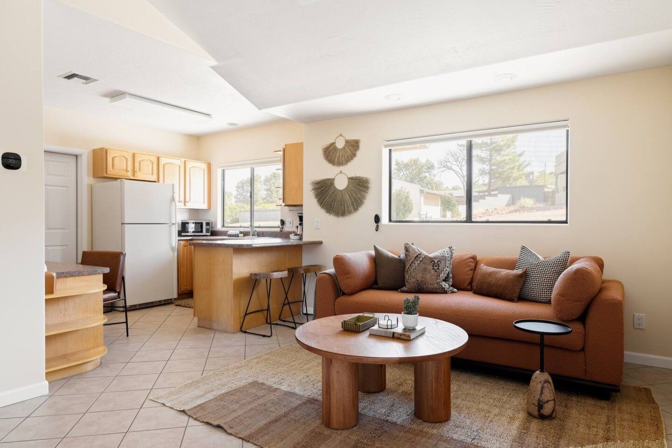 Een moderne keuken met een centraal eiland, een zithoek met een bruine leren bank en een groot raam dat zorgt voor veel daglicht.