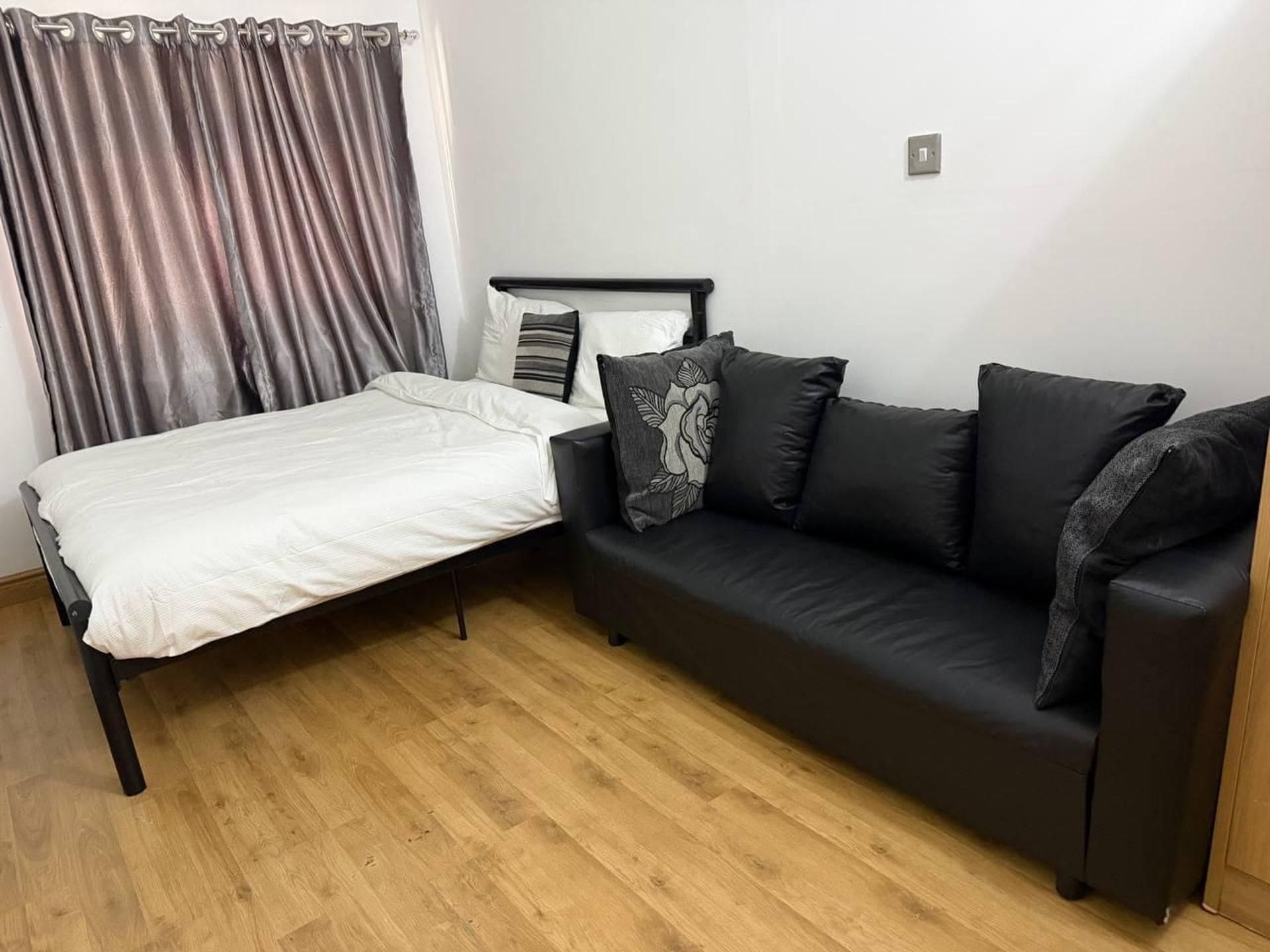 Una habitación con una cama, un sofá negro y piso de madera.
