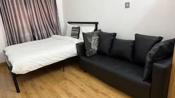 Una habitación con una cama, un sofá negro y piso de madera.