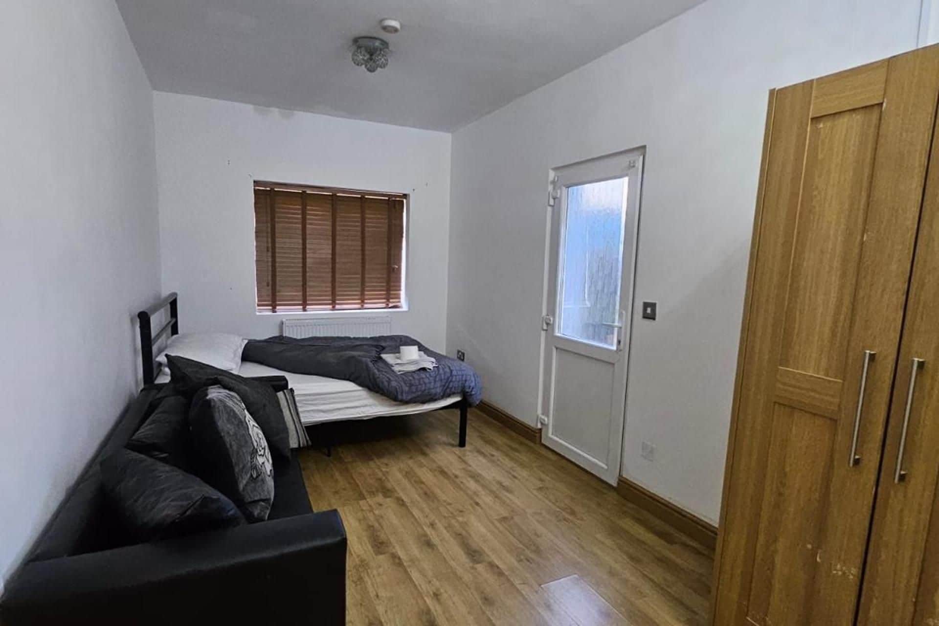 A compact room with a bed, a wooden wardrobe, a radiator, and a window with blinds.