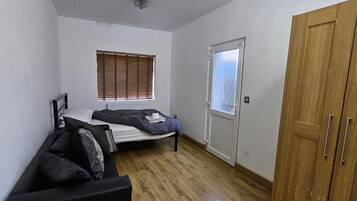 A compact room with a bed, a wooden wardrobe, a radiator, and a window with blinds.