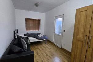 Una habitación pequeña con cama, un armario de madera, un radiador y una ventana con persianas.