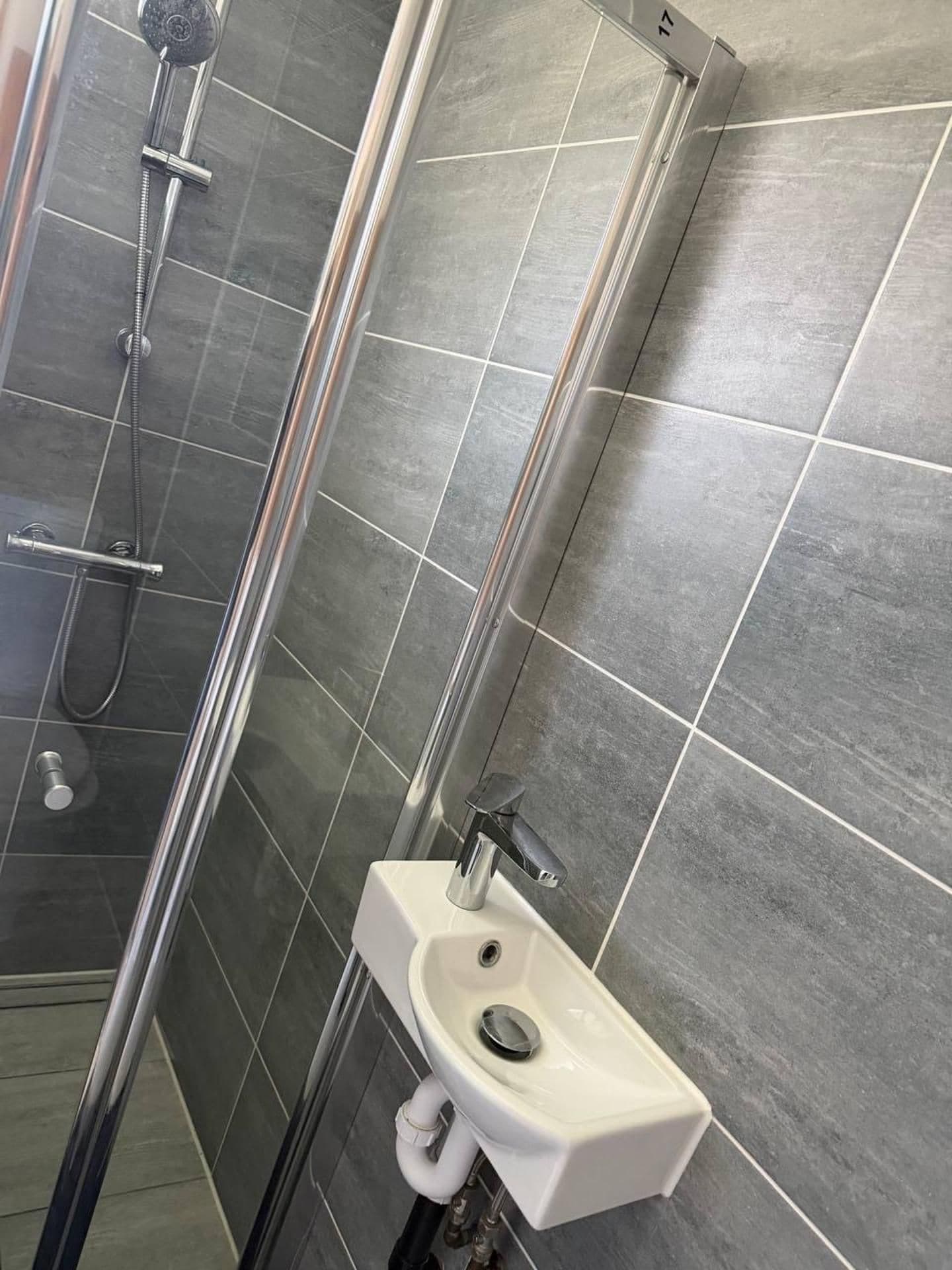 A modern bathroom with a glass shower enclosure, a white sink, and grey tiled walls.