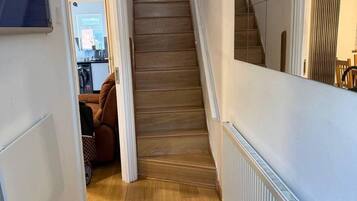 A hallway with a wooden staircase, a radiator, and a door leading to a room with a bed and a chair.