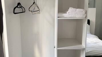 A white wardrobe with hanging space and shelves, a bed with white bedding, and a mirror.