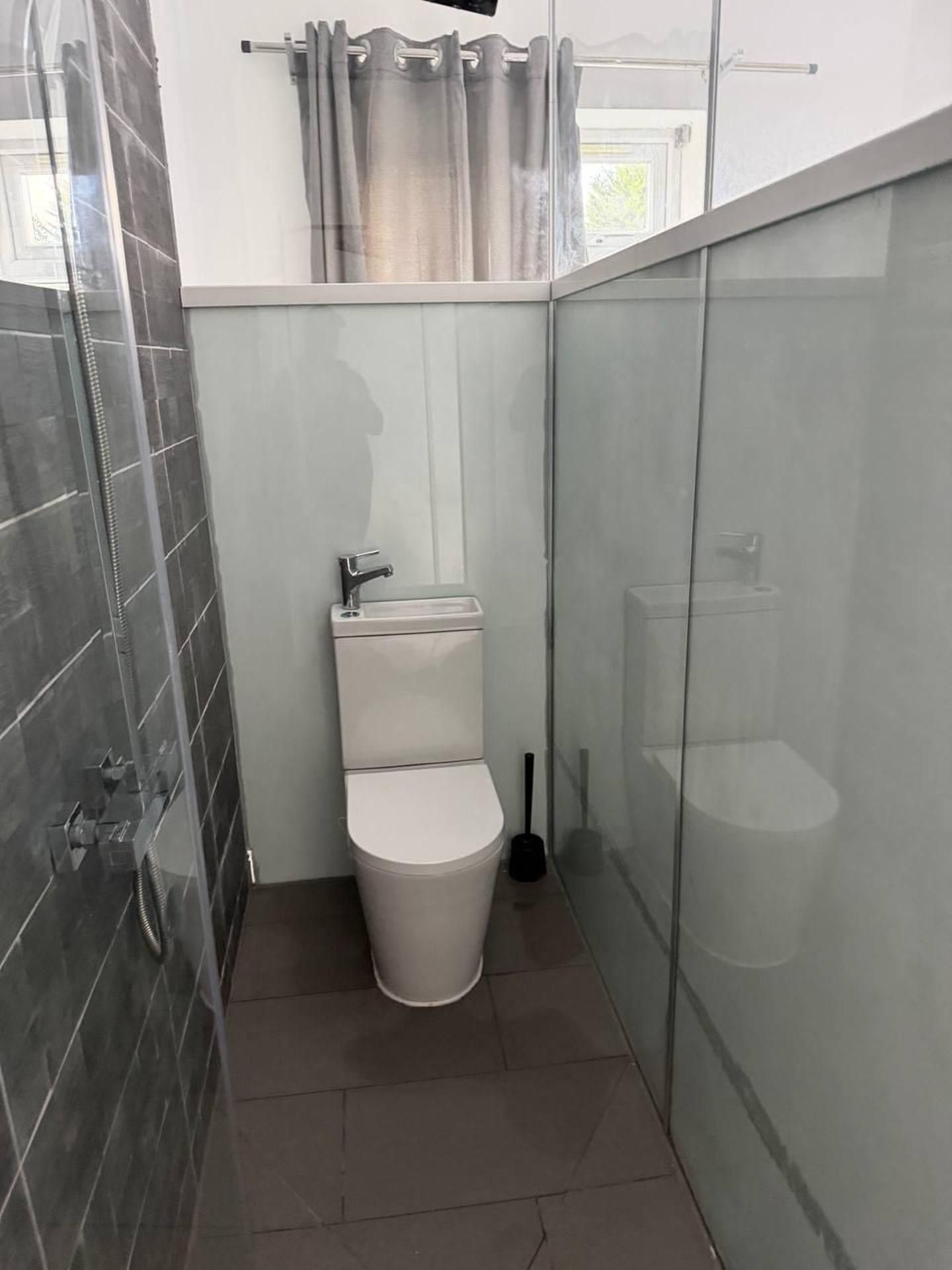 Un baño pequeño y cerrado con inodoro, ducha y lavamanos.