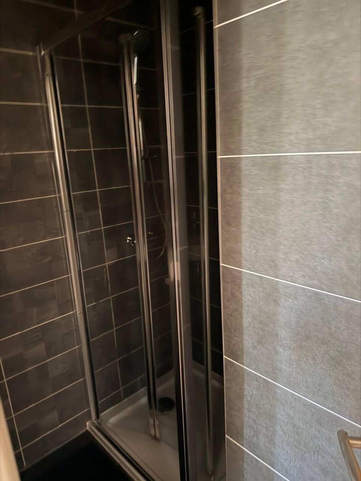 Aseo con cabina de ducha, puerta de cristal y pared con azulejos.