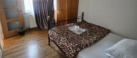 A bedroom with a bed, a wardrobe, a radiator, and a window with curtains.