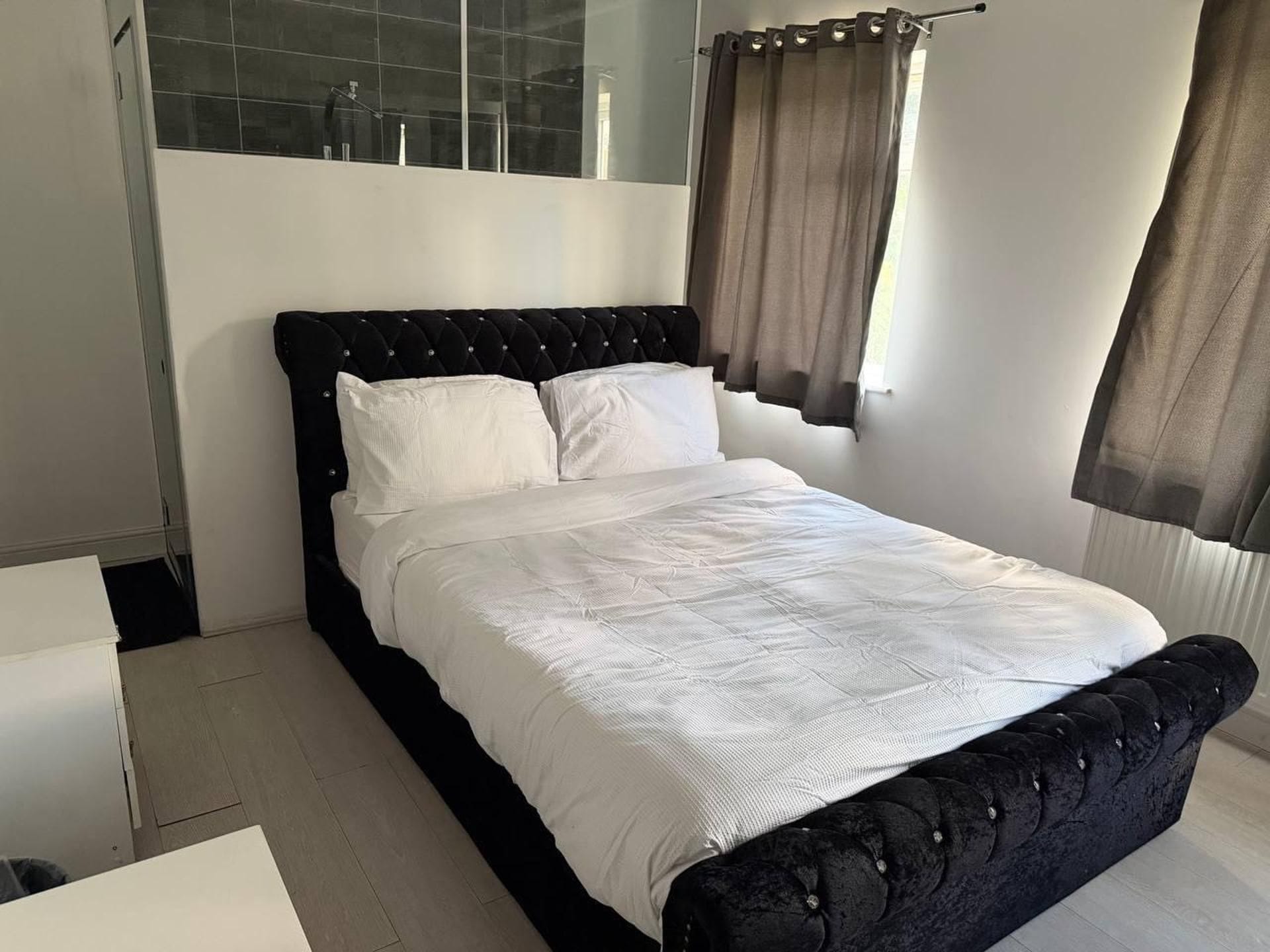 Un dormitorio moderno con un cabecero tapizado en negro, ropa de cama blanca y una mampara de ducha de vidrio.