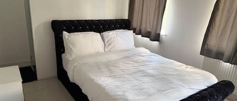 A modern bedroom with a black upholstered headboard, white bedding, and a glass shower enclosure.