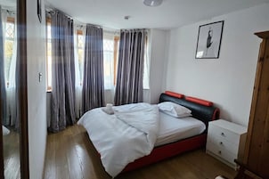 Un dormitorio con cama, mesita de noche, cómoda y ventana con cortinas.