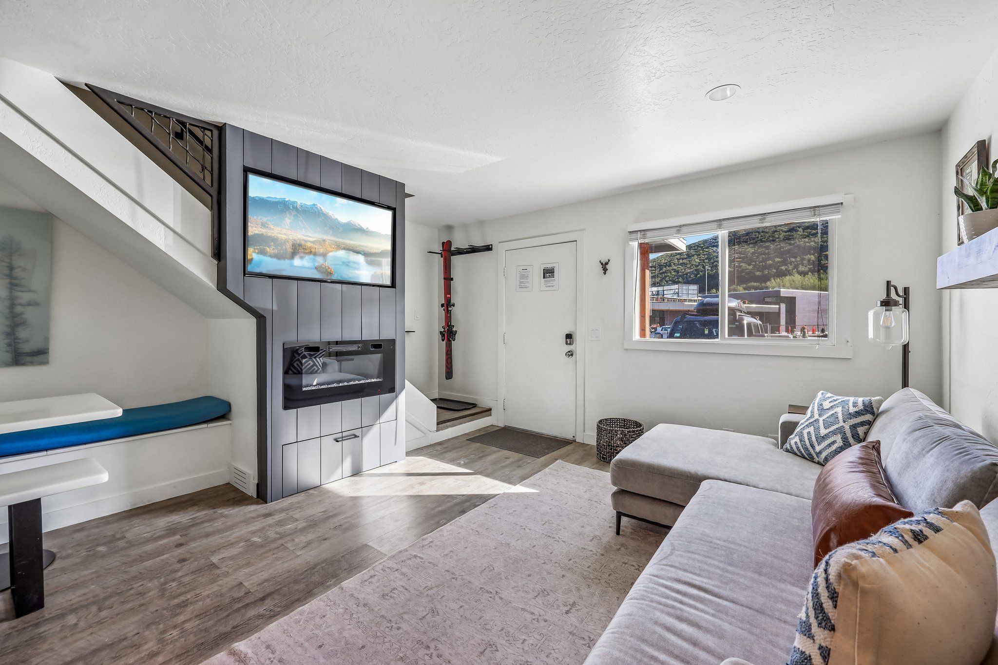 Ein modernes Wohnzimmer mit Flachbildfernseher, einer Couch, einer Treppe und einem Fenster mit Blick auf ein Gebäude.