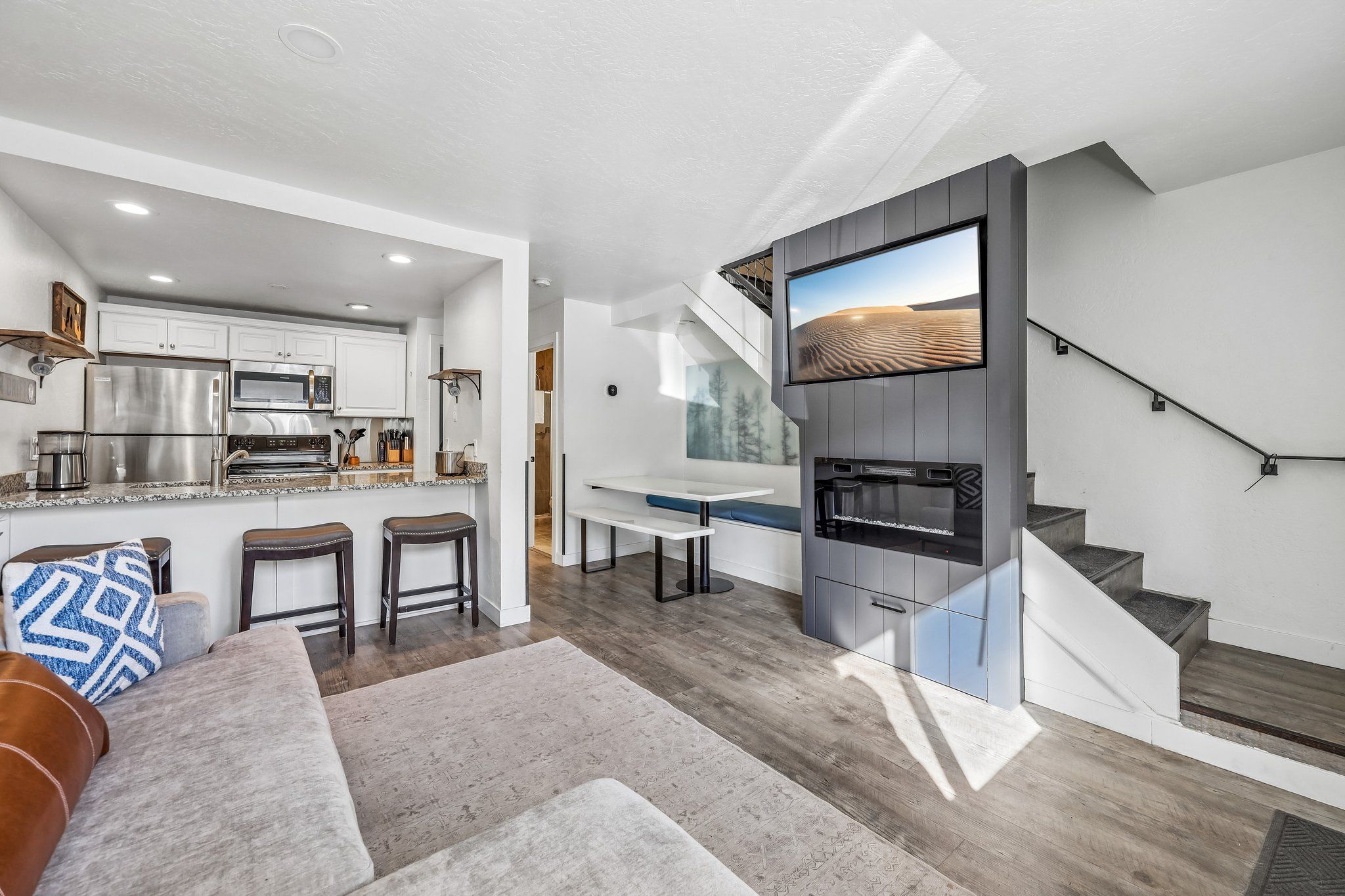 A modern kitchen with a built-in oven and microwave, a dining area with a bench, and a staircase leading to a loft.