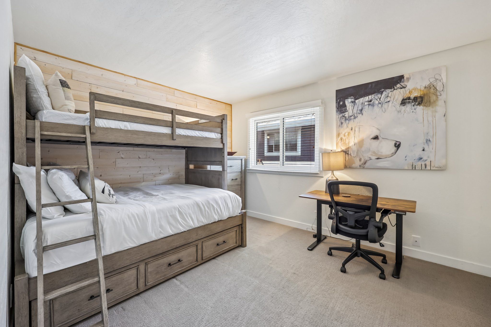 Quarto com beliche, escrivaninha e cadeira, e janela com persianas.