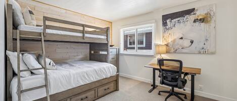 Quarto com beliche, escrivaninha e cadeira, e janela com persianas.