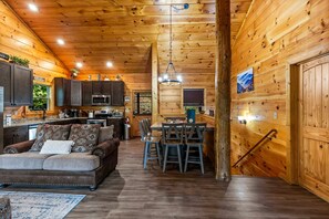 A cozy cabin interior with a kitchen, dining area, and a living room furnished with a sofa and chairs. - The Sporting Place - Outdoor Hot Tub, Firepit, Game Room + Close to Pigeon Forge (Sevierville)