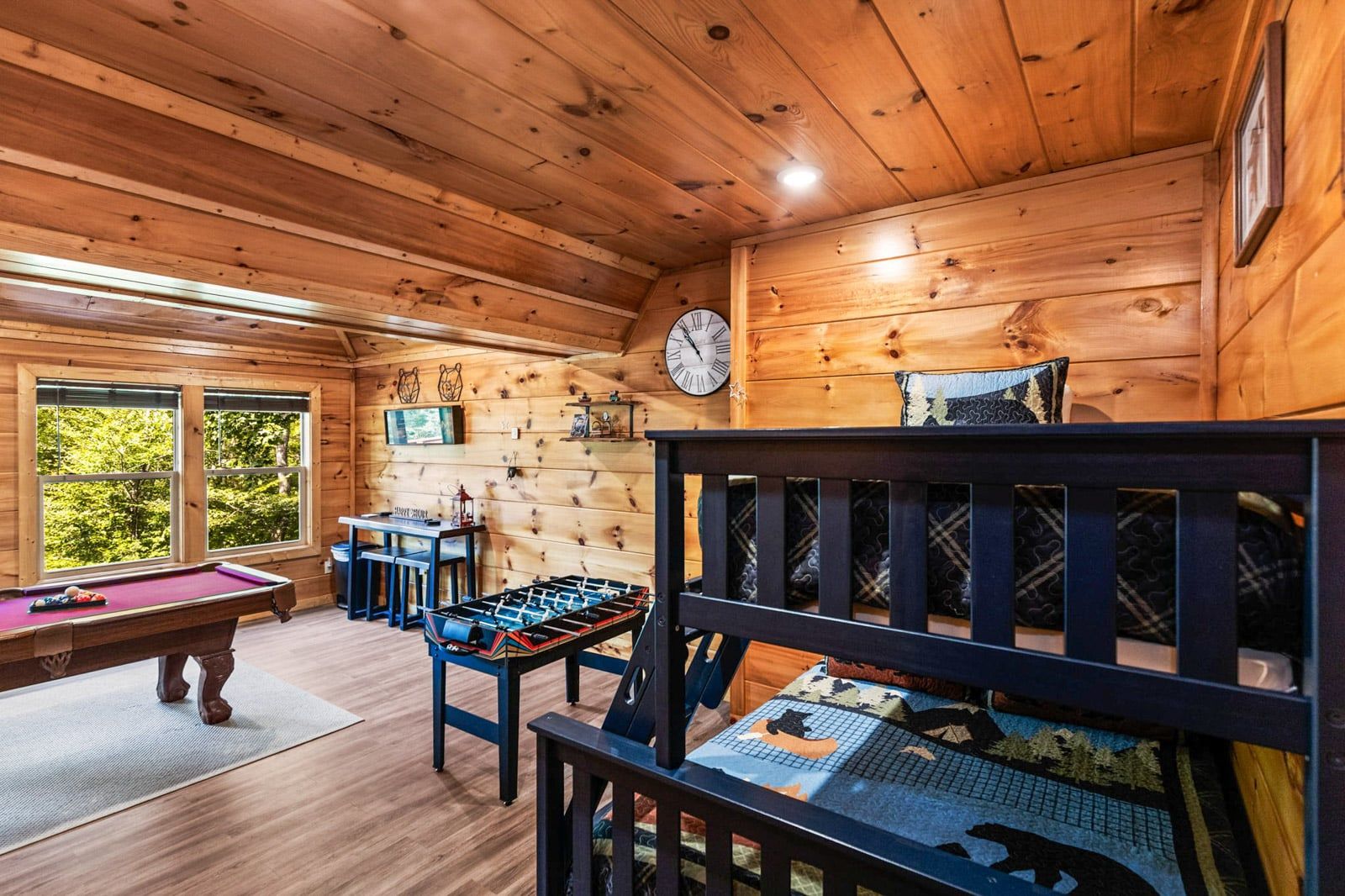 A wooden interior with a pool table, foosball table, and a bunk bed.