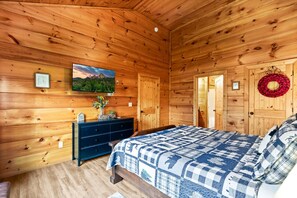 A wooden cabin bedroom with a bed, dresser, and a painting on the wall. - The Sporting Place - Outdoor Hot Tub, Firepit, Game Room + Close to Pigeon Forge (Sevierville)