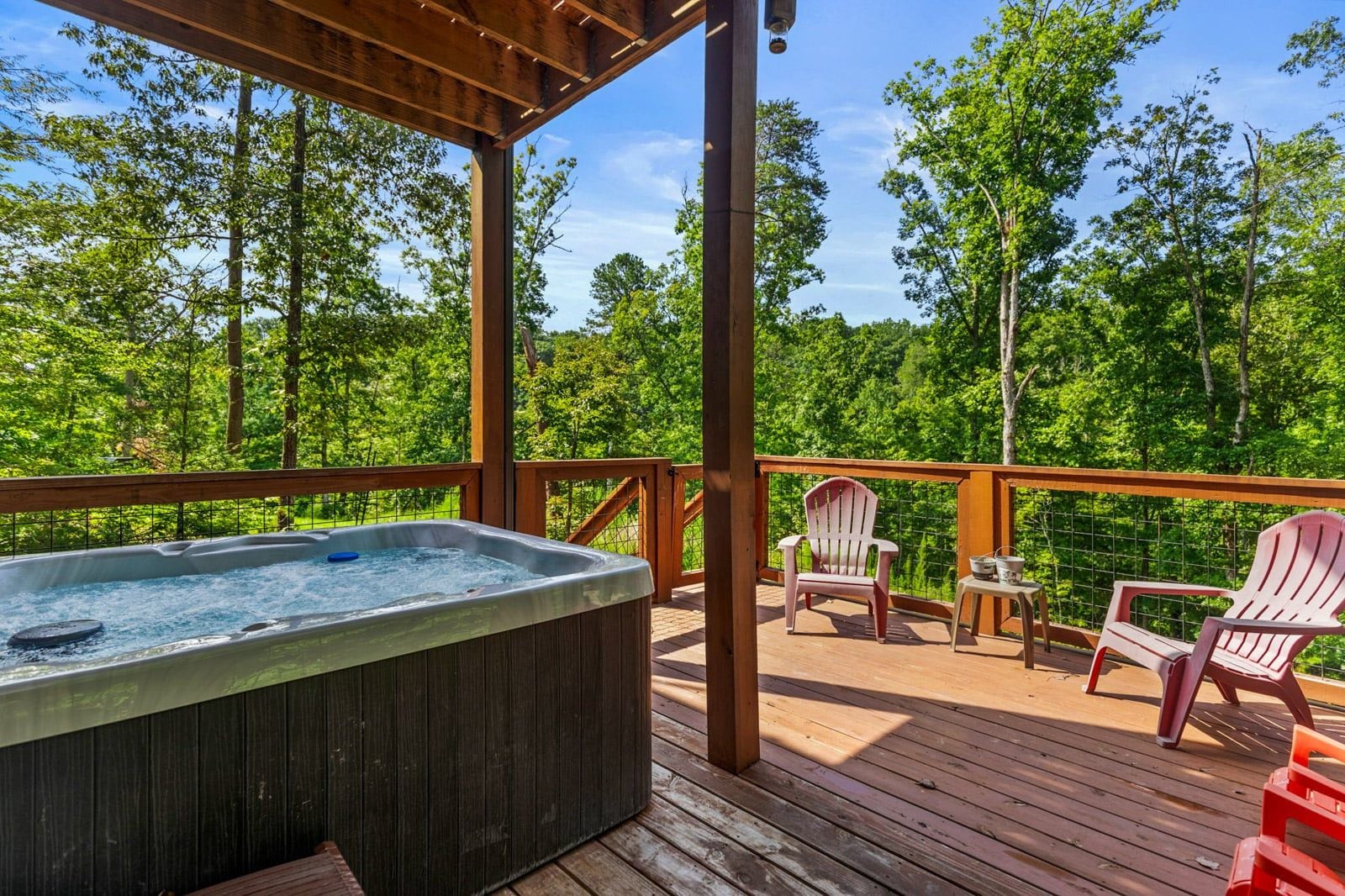 A hot tub on a wooden deck with chairs and a table, surrounded by trees.