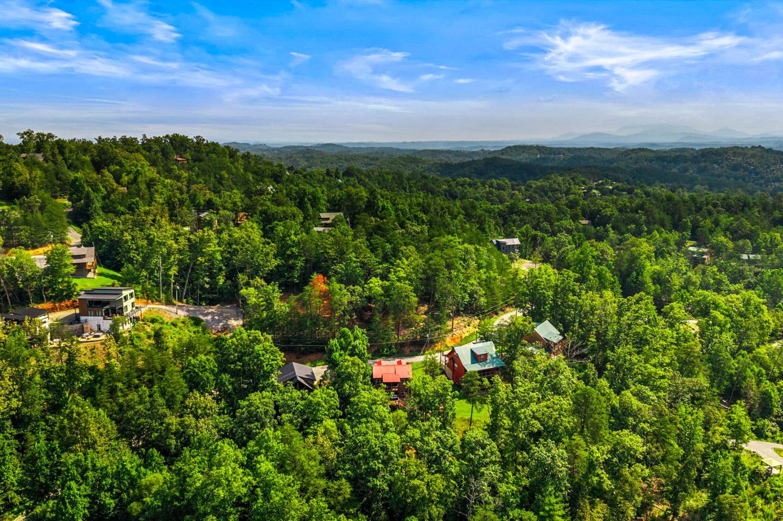 Um bairro residencial com várias casas rodeado por uma floresta densa, céu claro e montanhas ao longe.