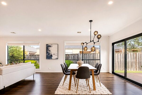 A modern dining area with a white table, black chairs, and a unique chandelier.