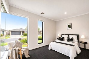 Une chambre d’hôtel avec une grande fenêtre, un lit avec du linge de lit blanc, une table de chevet avec une lampe et un tableau encadr é au mur.