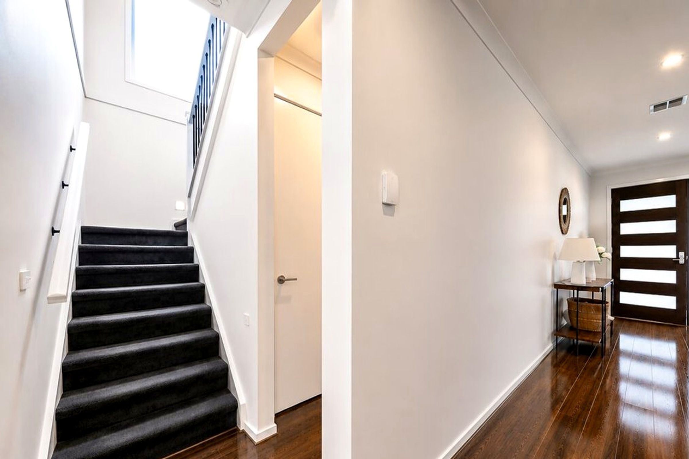 Un escalier menant à une porte équipée d’un interrupteur et d’un luminaire fixé au mur.