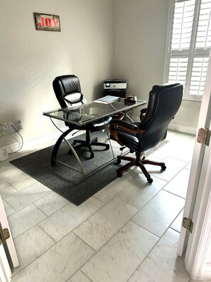 A conference room with a glass table, two black office chairs, a printer, and a motivational poster on the wall.