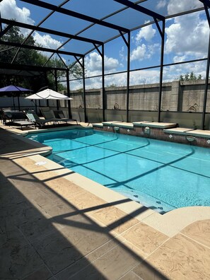 A swimming pool with a glass enclosure, sun loungers, and a stone-tiled deck.
