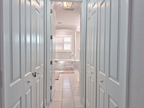 Corredor com portas brancas que dão para um banheiro com chuveiro e vaso sanitário.