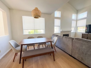 Un espacio habitable moderno con una mesa de comedor, sillas, un banco, un sofá gris y un televisor sobre un mueble de madera.