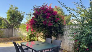 Un patio con tavolo e sedie, circondato dal verde e da una recinzione in legno.