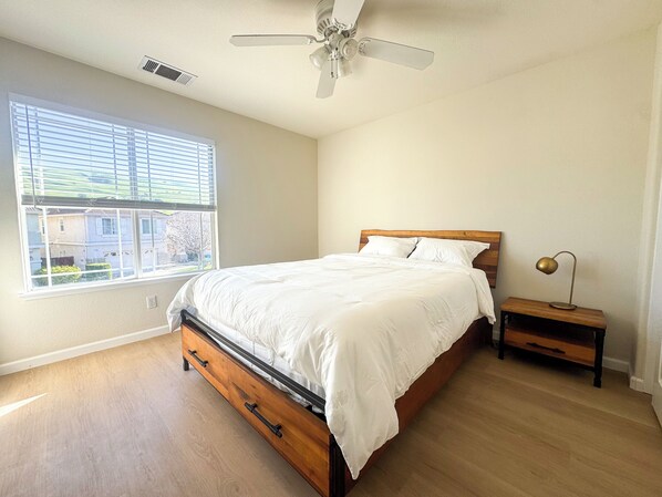 Une chambre à coucher avec un lit en bois, une table de chevet, un ventilateur de plafond et une fenêtre avec des stores.