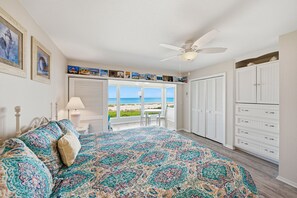 Une chambre avec un grand lit, un ventilateur de plafond, une vue sur la plage et un ensemble d’armoires blanches.