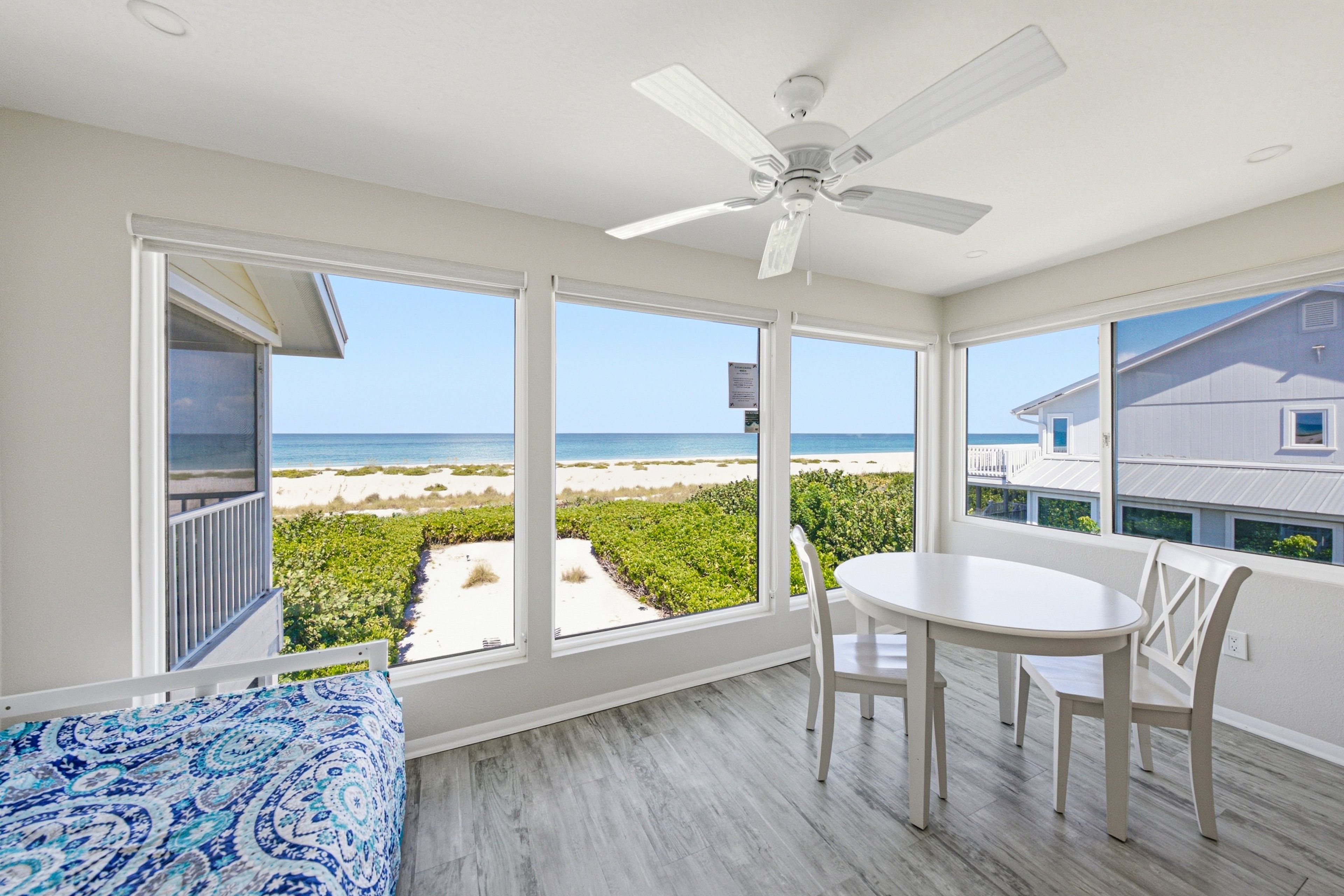 Une pièce dotée d’un ventilateur de plafond, d’une table à manger avec des chaises et de grandes fenêtres donnant sur la plage.