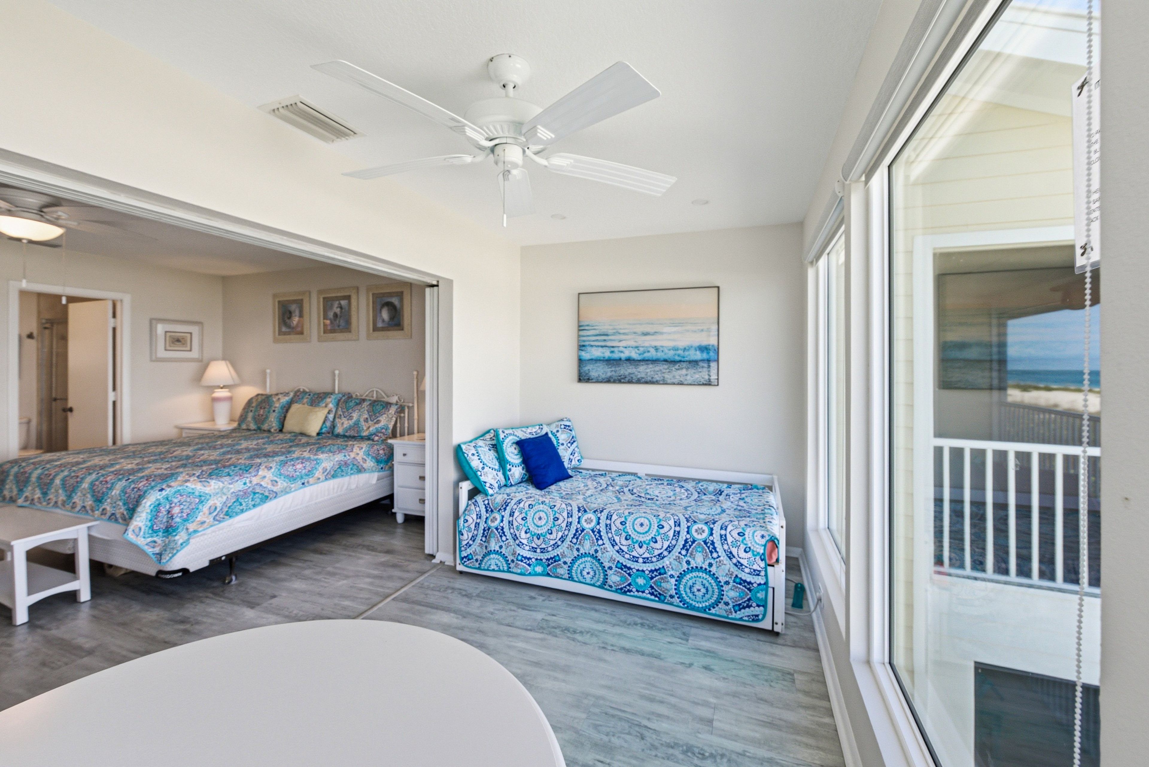 A bedroom with two beds, a ceiling fan, and a view of the ocean through a large window.