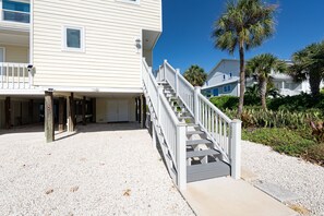 A beachfront property with a covered patio, a staircase leading to the entrance, and a palm tree in the background. - Gulf Dunes 1 | 2 Bed-2.5 Bath | Gulf Front | Pet friendly! | Sleeps 5 (Boca Grande)