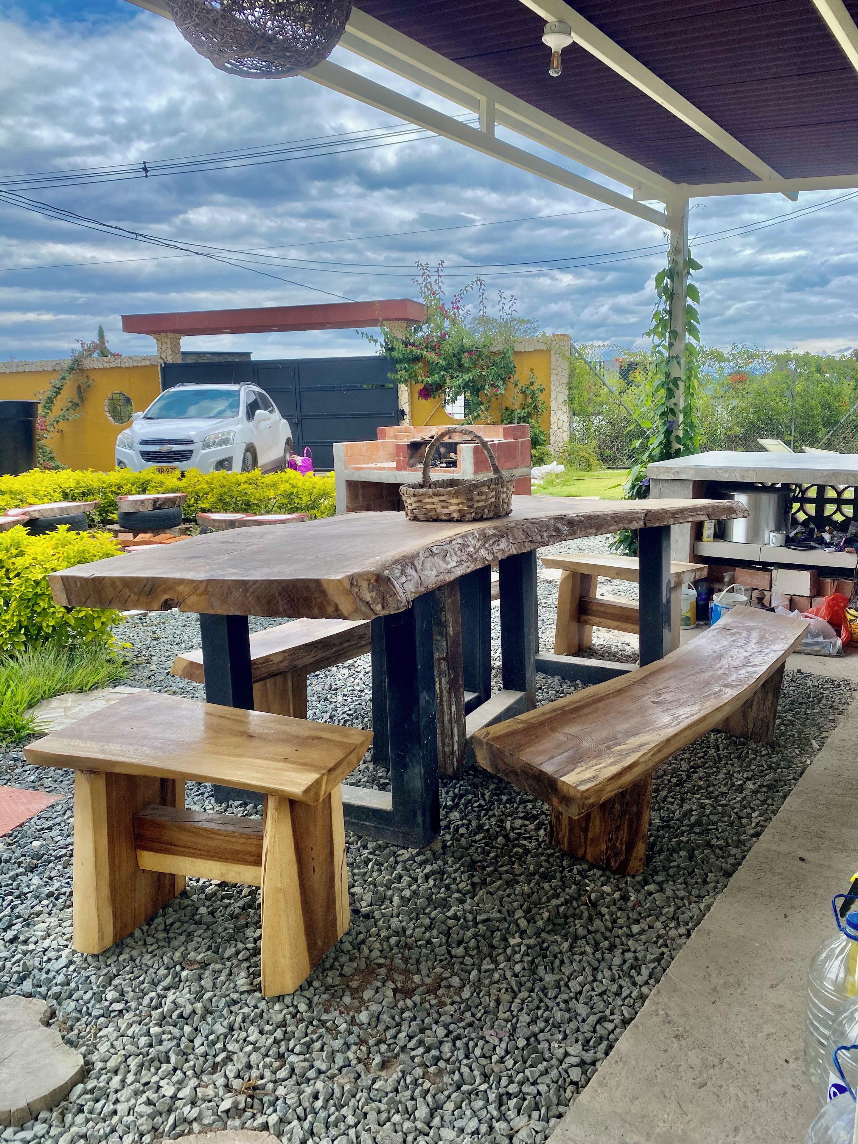 An outdoor patio with wooden benches and tables, surrounded by gravel and greenery.