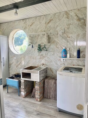 A kitchen with a built-in oven, a washing machine, and a window with a view of greenery. - Cozy Mediterranean Chalet (Alcalá)
