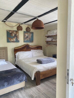 A bedroom with two beds, a wooden headboard, a hanging woven light fixture, and artwork on the wall.