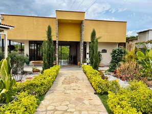 A modern building with a stone pathway leading to the entrance, surrounded by well-maintained gardens and a welcoming sign.