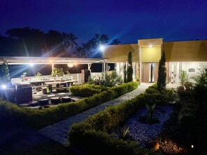 A well-lit outdoor patio area with a dining table, chairs, and potted plants.